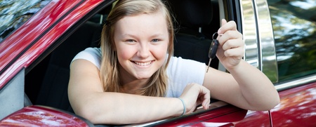 Ung kvinna sitter i en röd bil och håller upp en bilnyckel med ett leende.