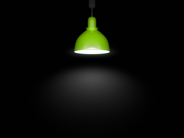En grön taklampa lyser upp ett mörkt rum med ett koncentrerat ljussken under sig.