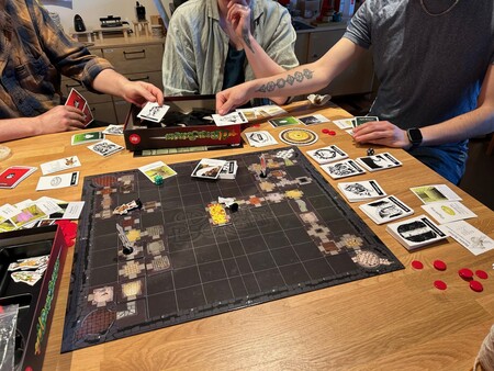 Tre personer spelar ett brädspel med kort och marker på ett träbord.