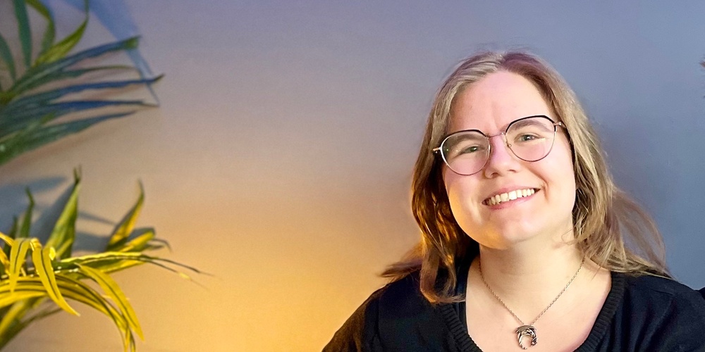 Två leende personer sitter tillsammans i en blå soffa i ett rum med blå vägg och grön växt.