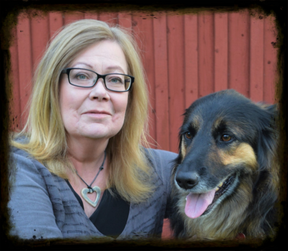Person med blont hår och grå tröja sitter bredvid en hund framför en röd trävägg.