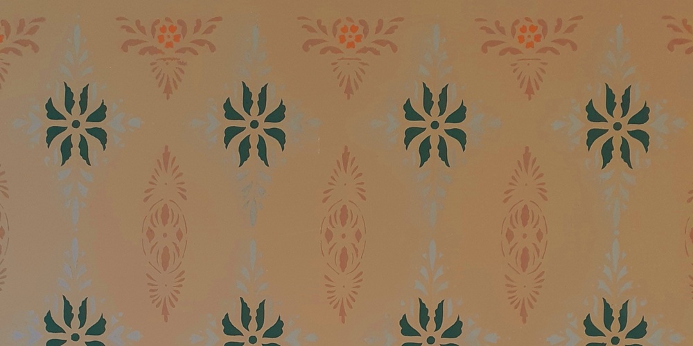 Vägg med symmetriskt mönster i grönt, orange och beige mot en ljus bakgrund.