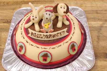 Födelsedagstårta dekorerad med figurer av en kanin, hund och mus, samt japansk text.