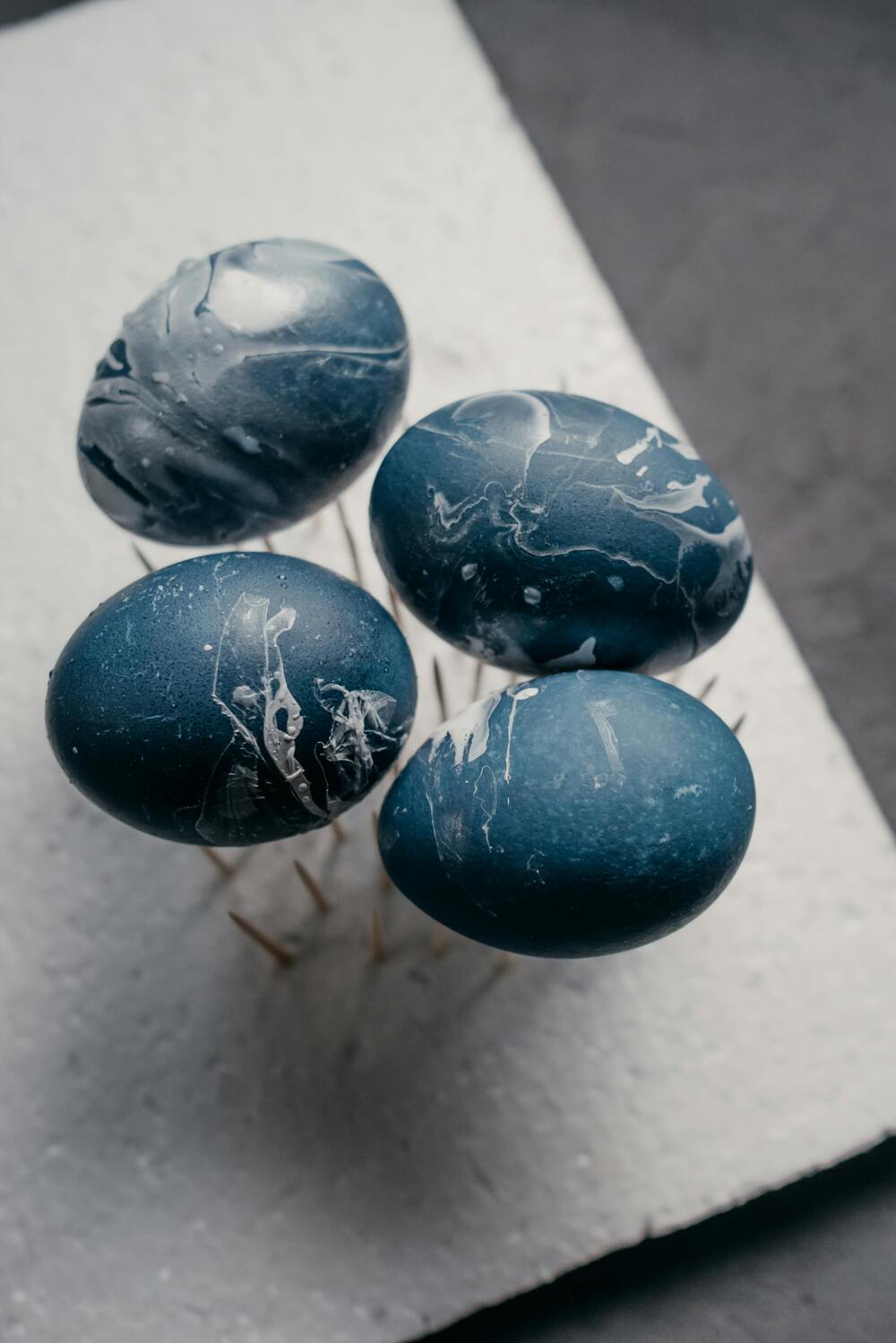 Fyra blå marmorerade ägg står på tandpetare i en bit vit frigolit.