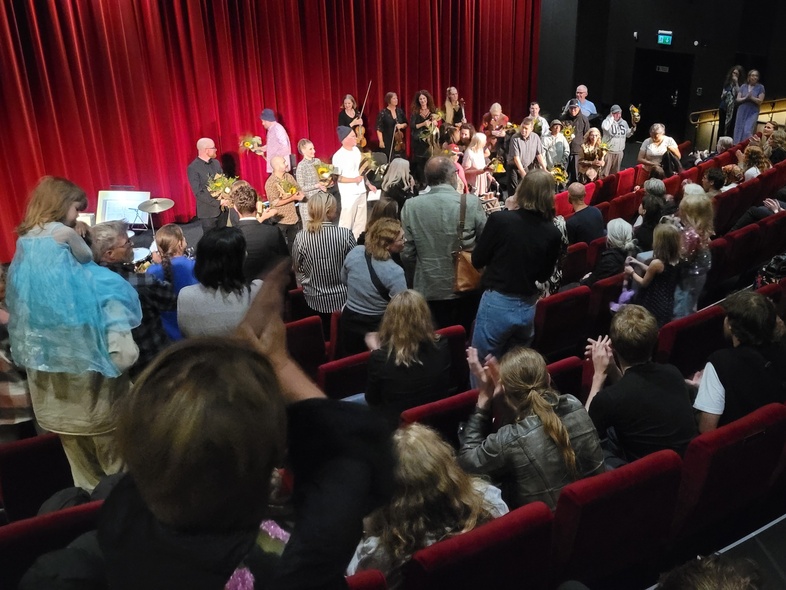 Bilden visar publiken sett bakifrån i en Biosalong på Panora i Malmö. Längst fram står skådespelarna, musikerna och filmteam.