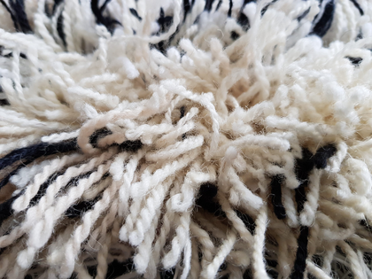 Närbild av en lurvig, vit och svart ullmatta med tjocka garntrådar.