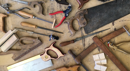 Ett urval av olika handverktyg för träarbete ligger utspridda på ett slitet träbord.