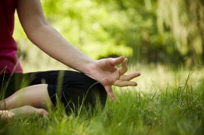 En person sitter i gräset och mediterar utomhus med handen i en yogaposition.