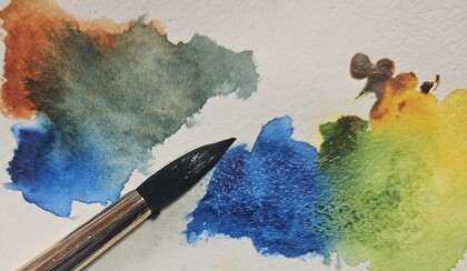 Närbild av en pensel och färgglada akvarellfläckar på papper.