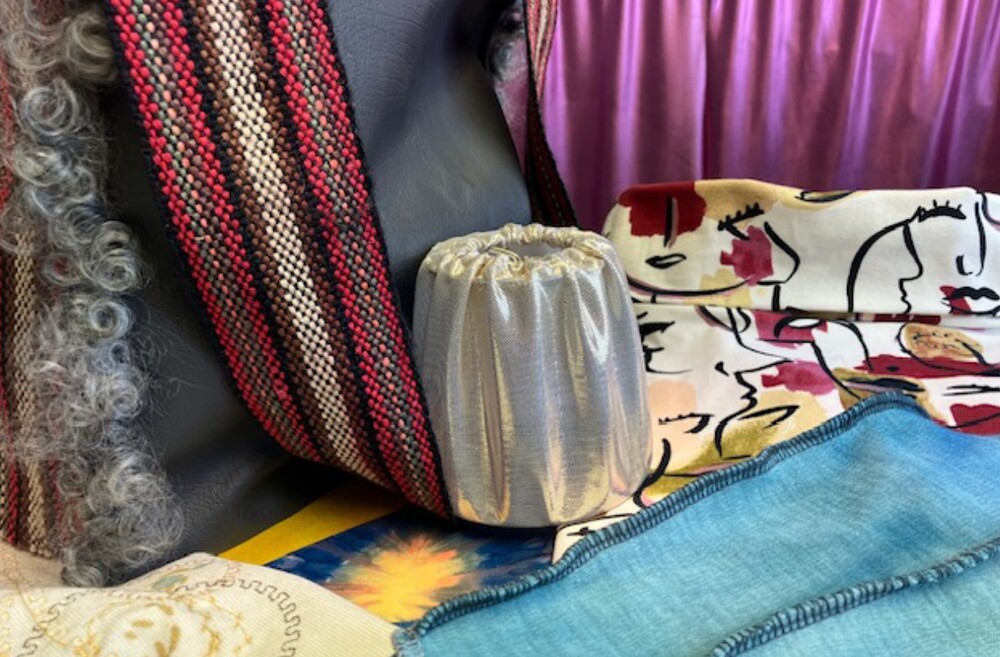 Olika tyger i olika färger och mönster, inklusive ett tyg med ansiktsmotiv och ett silverfärgat tygstycke.