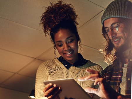 Två personer samarbetar vid en surfplatta i ett kontorsutrymme med dämpad belysning.