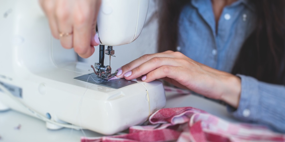 En person syr tyg med en symaskin, händerna syns tydligt vid arbetet.
