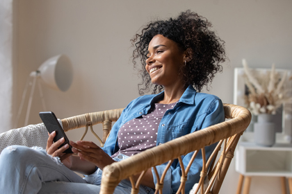 Person sitter avslappnat i en rottingstol och använder en smartphone i ett ljust vardagsrum.