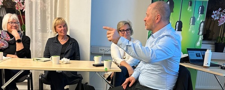 Fyra personer från Demokratiskolan sitter runt ett bord i ett mötesrum på SV Bollnäs och samtalar, en man gestikulerar medan han pratar.