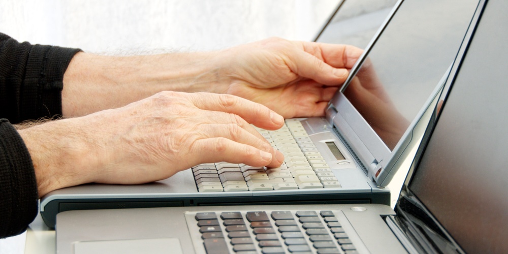 Två bärbara datorer används samtidigt av en person som skriver på tangentbordet.