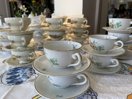 Flera staplade porslinskupor och fat står på ett dukat bord med blommigt mönster.