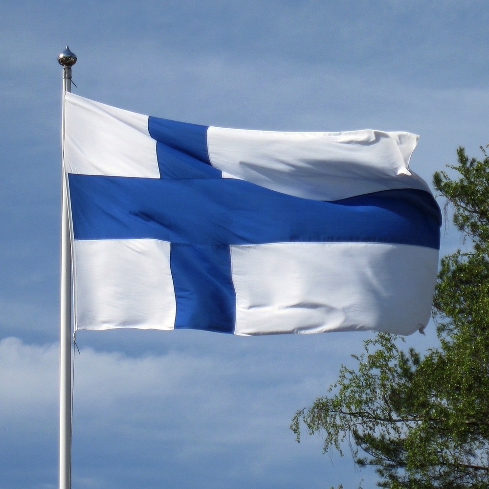 Finlands flagga vajar utomhus mot en blå himmel med några träd i bakgrunden.