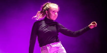 En person dansar barfota på en scen med lila ljus och rökeffekter.