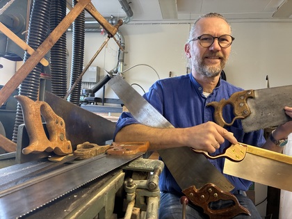 Person i blå skjorta håller flera olika handsågar i en verkstad med träbearbetningsverktyg.