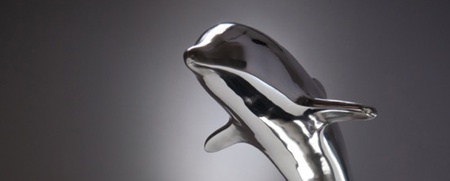 En silverfärgad delfinstatyett på en svart bas, placerad på ett blankt bord med mjuk belysning.