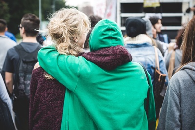 Två personer står tätt tillsammans i en folkmassa, en med grön hoodie har armen om den andra.