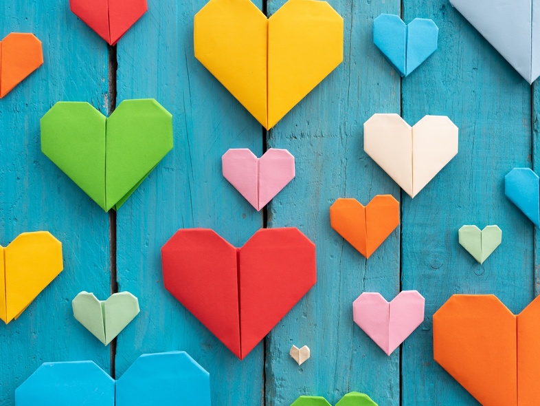 Flera färgglada origamihjärtan i olika storlekar på en blå träbakgrund.