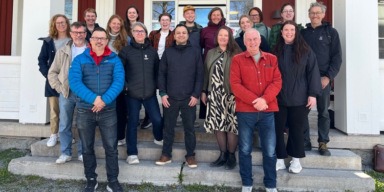 En grupp människor står utomhus framför en röd och vit byggnad, poserar för ett gruppfoto.
