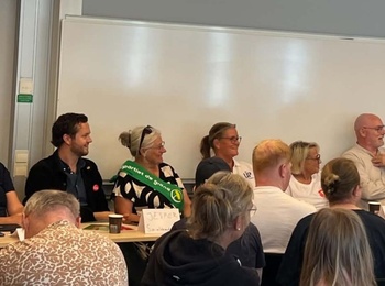 Paneldebatt med flera personer sittande vid ett bord och publik framför, i ett klassrum.