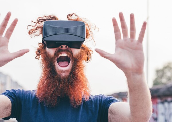 En man med rött hår och skägg har VR-glasögon på sig och håller upp händerna framför sig.