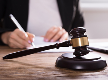 En domarklubba ligger på ett skrivbord medan en person skriver på papper i bakgrunden.