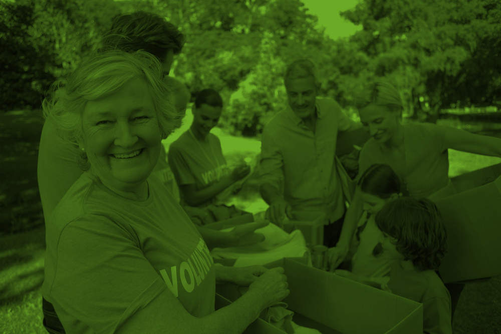 En grupp människor, inklusive en äldre kvinna som ler, packar lådor utomhus i en park.