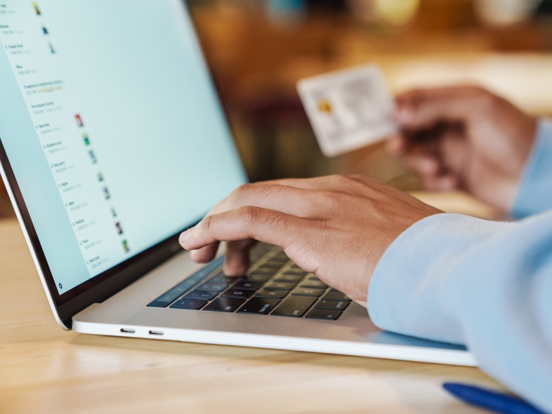 En person använder en bärbar dator och håller ett kreditkort, troligen för onlineköp.