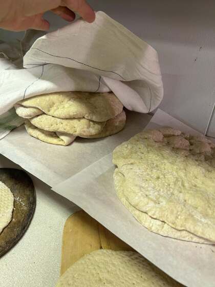 Flera platta klådda bröd ligger på bakplåtspapper och täcks av en kökshandduk, en hand lyfter på duken.