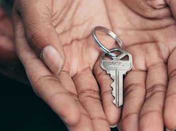 Två händer håller tillsammans en nyckel på en nyckelring, fokus på händer och nyckel.