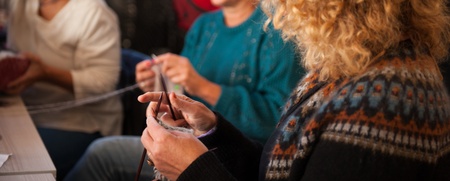 Tre kvinnor sitter tillsammans och stickar med garn och stickor i en varm, inomhusmiljö.