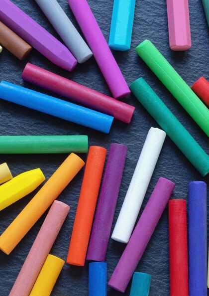 Flera färgglada kritor ligger utspridda på en mörk yta.