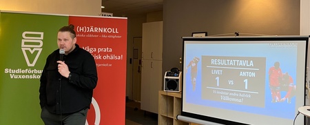 Person håller mikrofon och står framför rollups och en projektorduk med resultat på svenska.