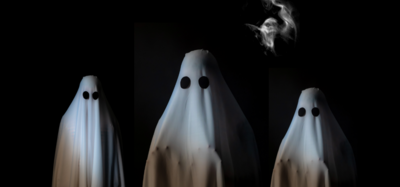 Tre personer utklädda till spöken med vita lakan och svarta ögon på en mörk bakgrund.