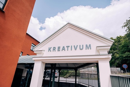 Entré till byggnad med skylten 'KREATIVUM' under blå himmel och vita moln.