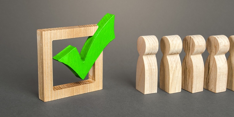 Träfigurer står bredvid en stor grön bock i en träram mot grå bakgrund.