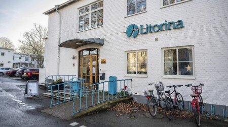 Entré till en vit tegelbyggnad med skylten 'Litorina', cyklar parkerade utanför och bilar på parkeringen.