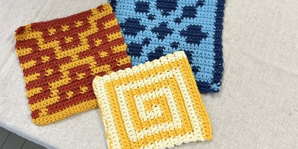 Tre virkade grytlappar med olika mönster och färger ligger på ett bord.