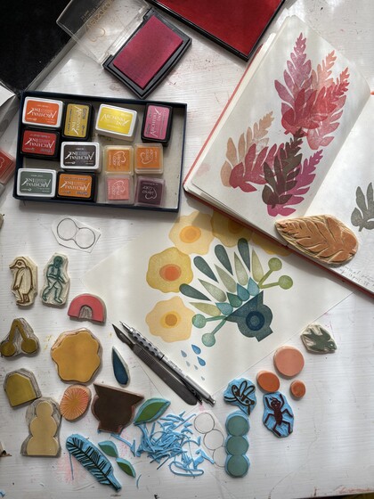 Ett skrivbord med stämplar, färgkuddar, verktyg och en öppen skissbok med bladmotiv.