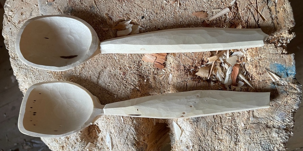 Två handgjorda träslevar ligger på en trästubbe med träspån runtom.