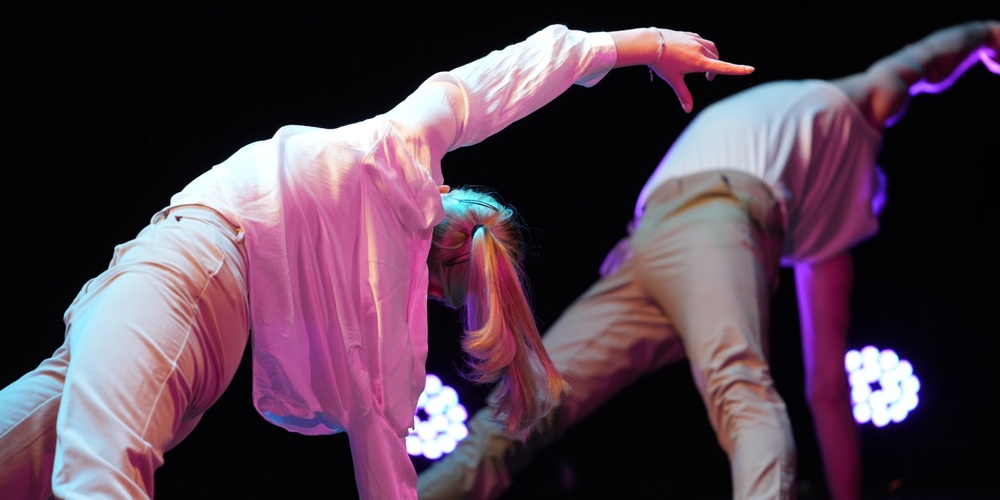 Två personer utför en modern dansrörelse på scen med färgglad belysning.