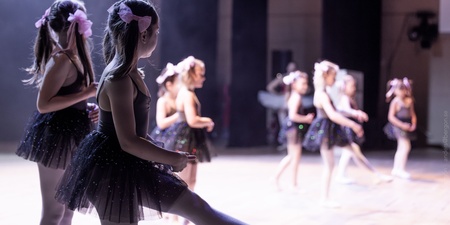 Flera unga flickor i svarta balettklänningar dansar på en scen med mjukt ljus.