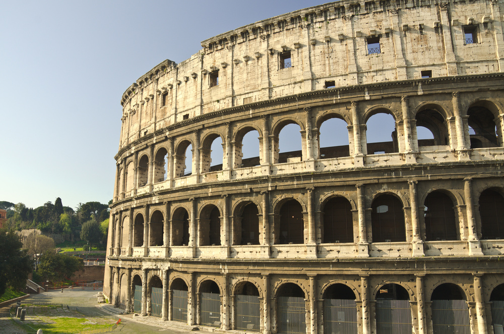 Närbild av Colosseum i Rom, en antik amfiteater med flera valvbågar och stenväggar under klar himmel.