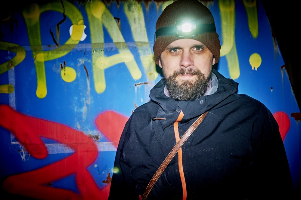 Person med mörk jacka och mössa står framför färgglad graffitivägg utomhus.