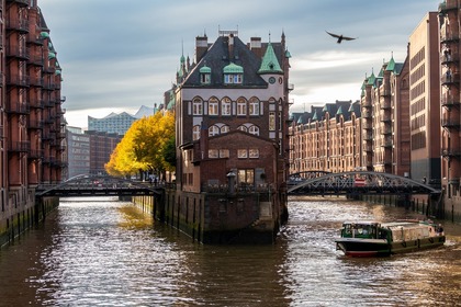 En kanal med en båt, omgiven av tegelbyggnader och ett hus på en ö, under en molnig himmel.