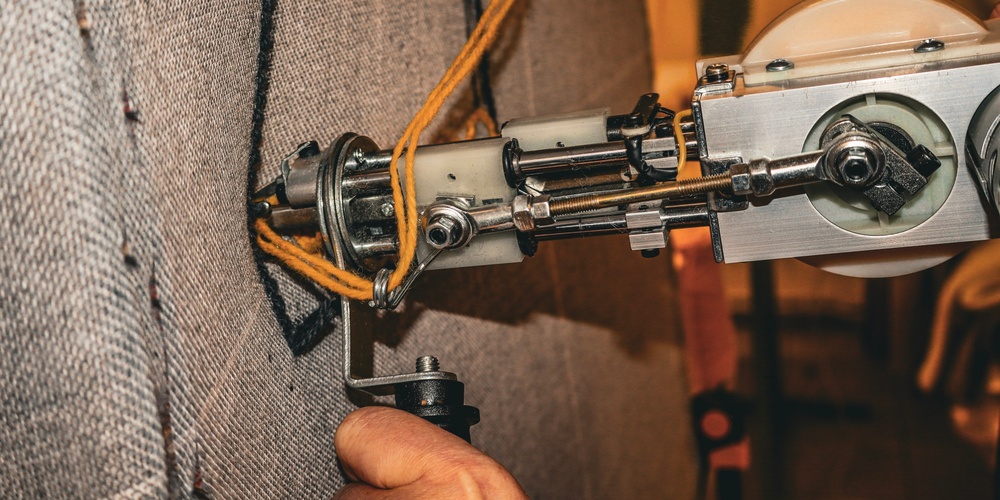 En tuftningsmaskin används för att sy garn i ett tyg, hand syns hålla i maskinen.